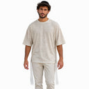 Homme portant le t-shirt Tsitsit Effet Lin beige Eliorness, vue de face sur fond blanc : coupe oversize, épaules tombantes, zips latéraux et tsitsit blancs aux quatre coins.
