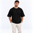 Homme portant le t-shirt Tsitsit Effet Lin noir Eliorness, vue de face sur fond blanc : coupe oversize, zips latéraux noirs et tsitsit blancs.